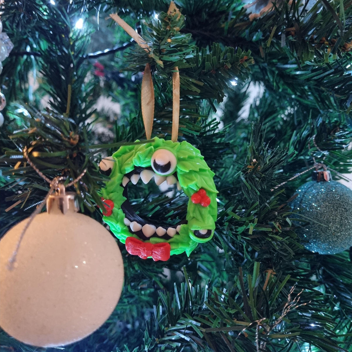 A Christmas tree decorated with ornaments, including a green wreath-shaped ornament with a monster-like face and a white ball ornament.
