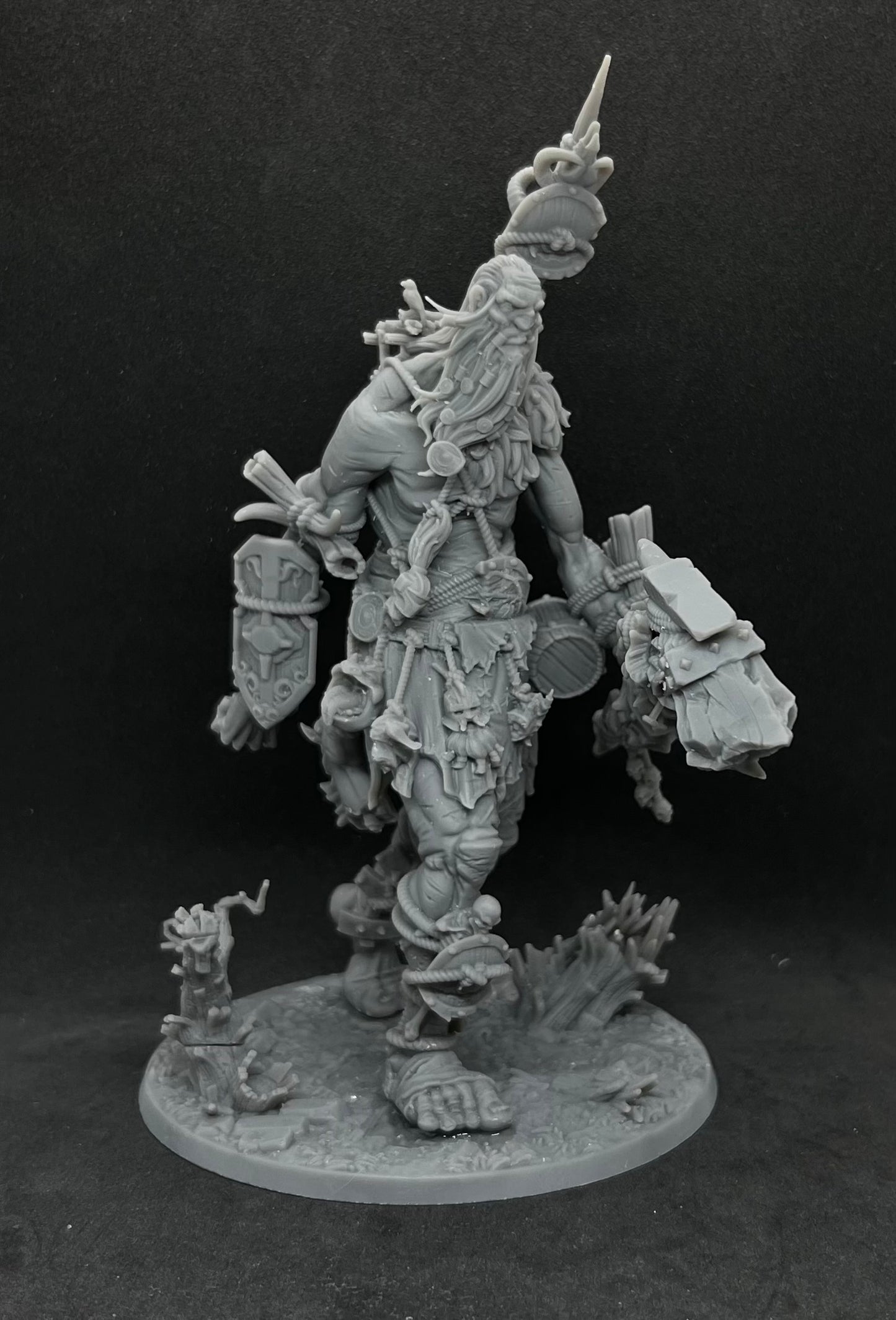 A detailed, intricate figurine of a fantastical creature with a long beard and various weapons, standing on a base and surrounded by smaller figurines.