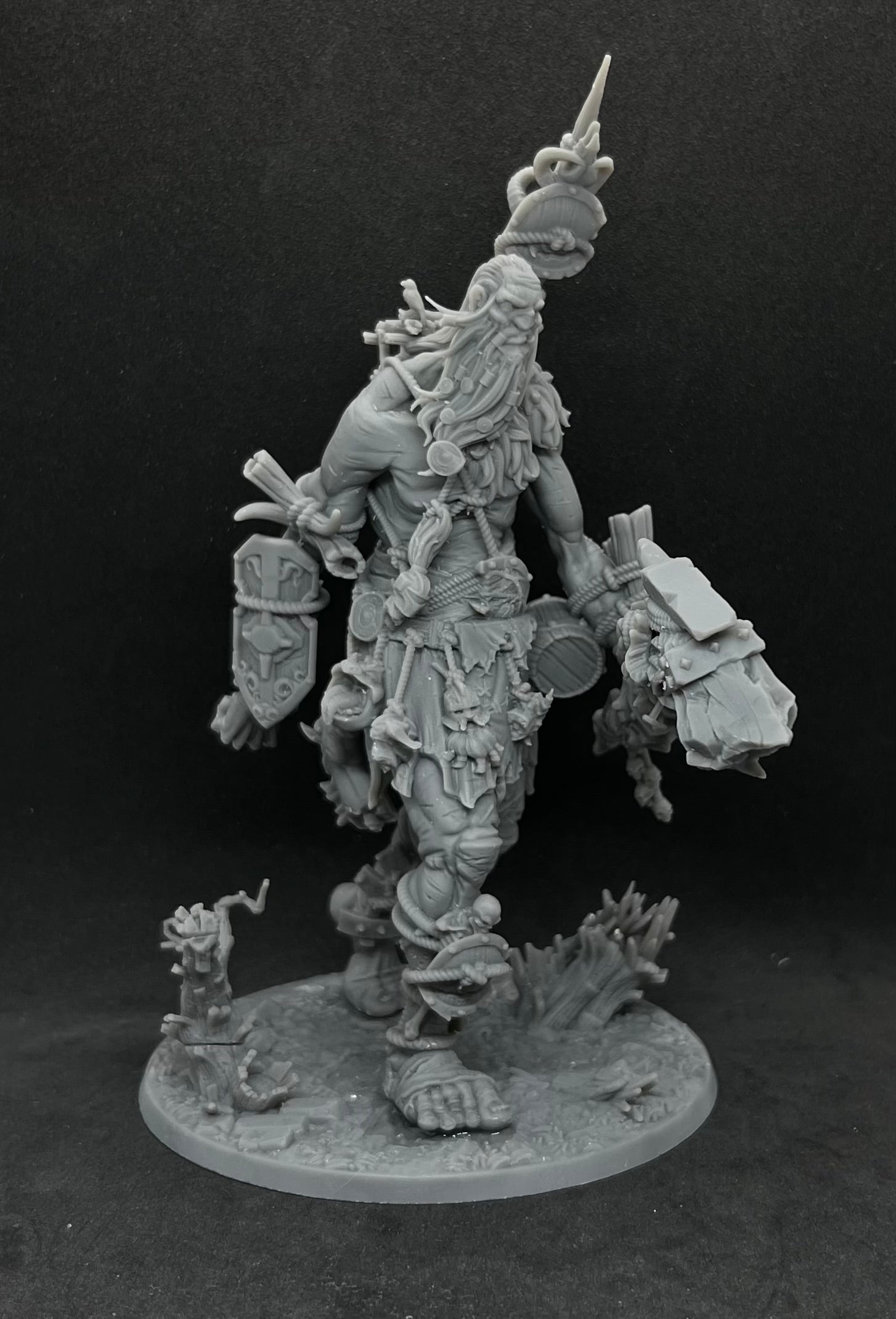 A detailed, intricate figurine of a fantastical creature with a long beard and various weapons, standing on a base and surrounded by smaller figurines.