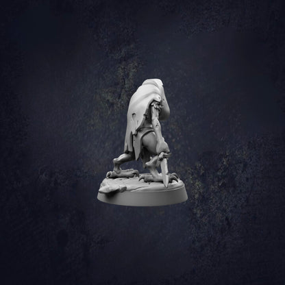 A white figurine of a person kneeling on a rock, with a cape or garment draped over their body, against a dark background.