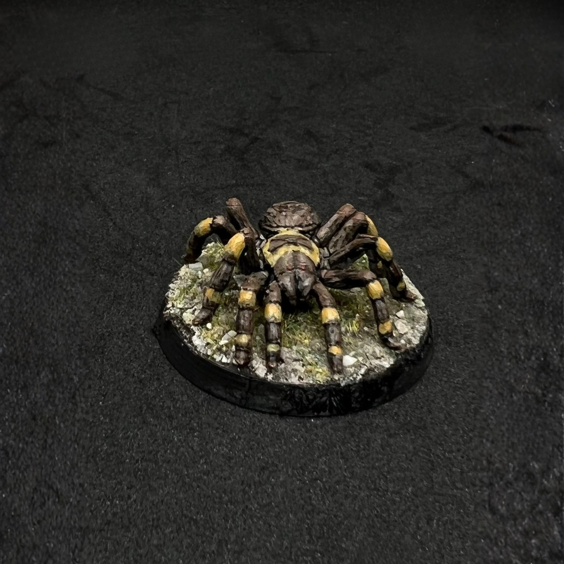A detailed model of a spider with yellow and brown markings on its legs and body, sitting on a black base.