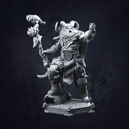 A detailed miniature of a barbarian warrior, featuring a bearded figure wearing a horned helmet. The barbarian wields a staff topped with a bird and is dressed in rugged attire, including fur-lined boots and a belt with a circular emblem. The figure stands on a textured base, exuding a dynamic and imposing presence.
