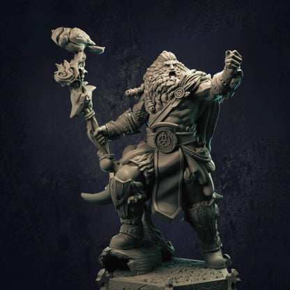 A meticulously crafted miniature figure of a barbarian Viking warrior standing on a rugged, rocky base. The character boasts a powerful, muscular physique, with wild, flowing hair and a full beard. Adorned in traditional Viking attire, the warrior's belt features a prominent circular emblem. He wields a striking staff crowned with a bird sculpture and intricate carvings, emphasizing his commanding presence. 