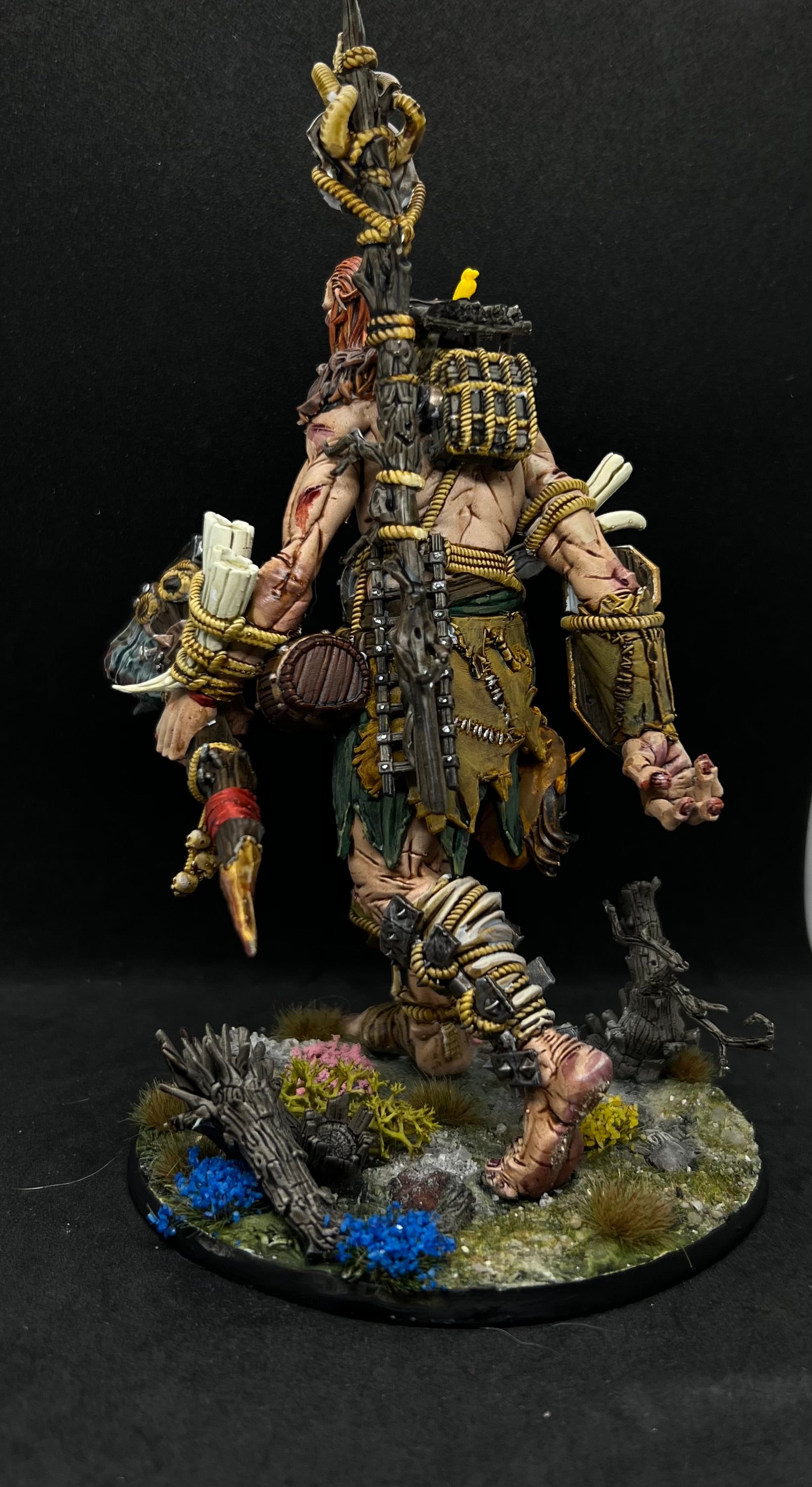 A detailed and intricate model of a fantasy character, possibly a warrior or monster, standing on a base with various accessories and weapons.