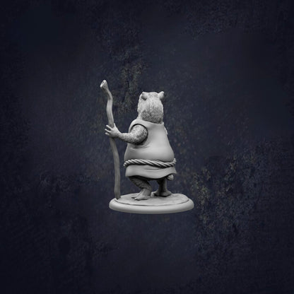 A small statue of a bear holding a stick and standing on a platform against a dark background.