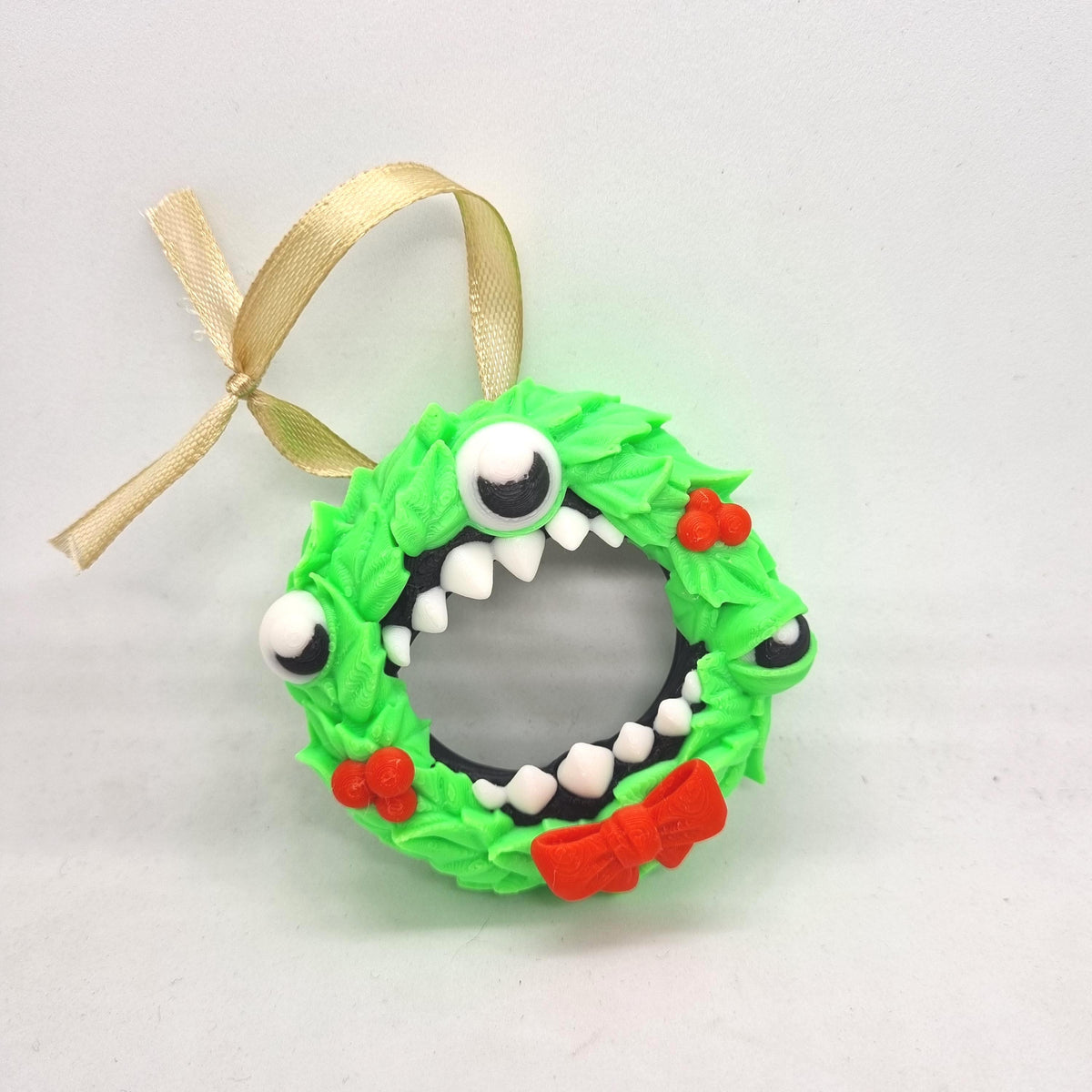 A green wreath ornament with a red bow and white eyes, resembling a monster or monster-like creature.
